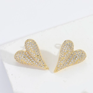 Detail of gold heart earrings with micro-set zircons on a white textured stone base