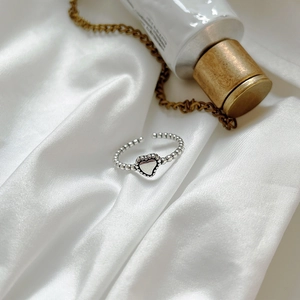 Close-up of vintage heart ring with beaded band on elegant white silk fabric