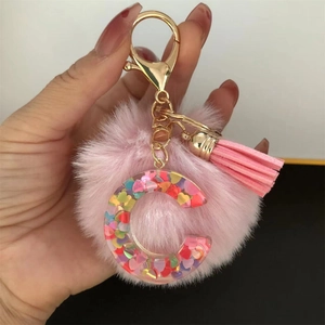 Detail of pink faux fur pom pom and resin letter C keychain with glitter heart sequins