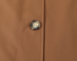 Nahaufnahme eines strukturierten Knopfes an einem braunen Mantel mit Twill-Stoffdetails