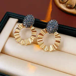 Elegant gold textured hoop earrings with oval blue pavé crystal studs on velvet