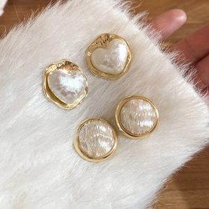 Dettaglio macro di orecchini a cuore e perla placcati oro 16K su sfondo di pelliccia