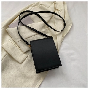 Mise à plat d'un sac à bandoulière noir minimaliste sur un blazer beige texturé