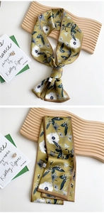 Elegant olive green silk scarf with large floral patterns styled on a wooden tray