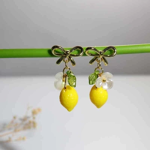 Detail of yellow lemon earrings with golden bow hooks, green leaves and small white flowers