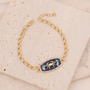 Macro detail of gold Cancer zodiac bracelet featuring blue enamel and purple zircon inlay