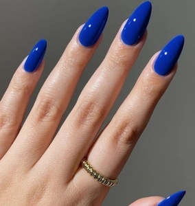 Détail d'ongles bleus brillants à effet miroir avec une bague spirale dorée chic