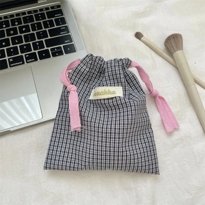 Close-up of black and white plaid drawstring storage bag with pink cotton rope and label