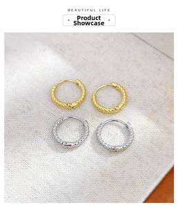 Detail of twisted rope hoop earrings in gold and silver finish on fabric background