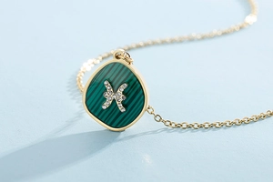 Detail showing gold Pisces zodiac pendant with malachite inlay and sparkling crystals