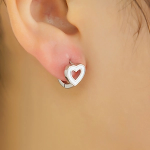 Gros plan d'une boucle d'oreille cœur en argent avec émail blanc portée par un mannequin
