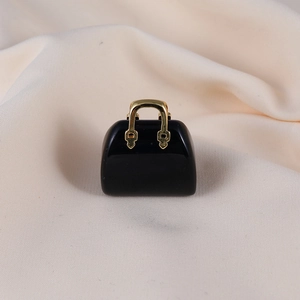 Detailed close-up of a black resin handbag pendant with gold handle on soft fabric
