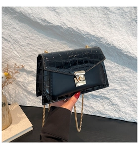 Detail of black faux crocodile skin flap and golden chain strap on a designer handbag