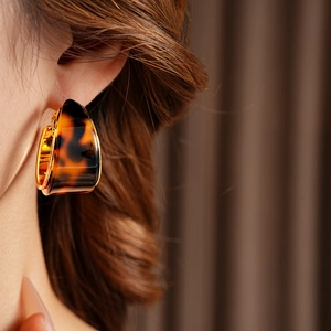 Close-up of model wearing gold-plated tortoiseshell resin hoop earrings with warm lighting