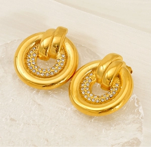 Macro detail of gold round earrings with crystal pavé on textured glass display tray