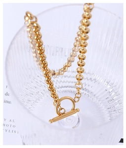 Close-up of golden chunky chain necklace with OT buckle on a textured glass