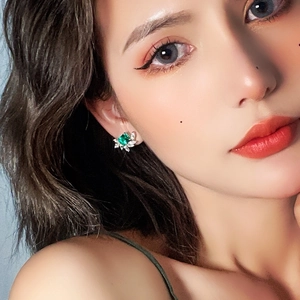 Elegant emerald-style flower stud earrings with green square gem on female model