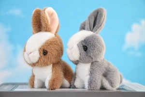 Detail of plush brown and grey rabbits sitting together against a blue sky background