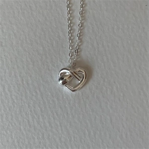 Macro view of a 925 sterling silver heart knot pendant on a white textured surface