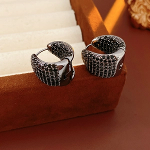 Close-up of C-shaped black cubic zirconia huggie earrings on a brown velvet box