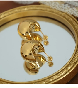 Close-up of golden chunky half-moon stud earrings with mirror polished finish on tray