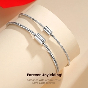Close-up of silver snake chain couple bracelets with unto engraved cylindrical pendant