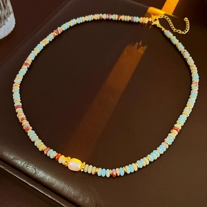 Close-up of colorful beaded necklace with a pink pearl pendant on a dark display