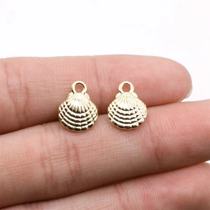 Detailed macro view of two gold shell charms held by fingers to show scale and texture