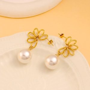 Elegant gold flower pearl earrings displayed on a white textured plate background