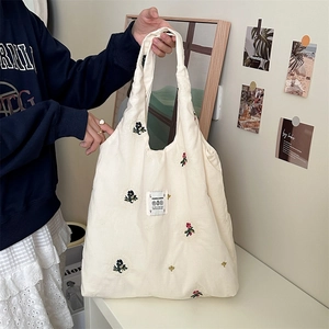 Detail of beige canvas tote bag with colorful flower embroidery and woven brand label