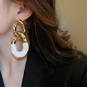 Détail de boucles d'oreilles ovales dorées texturées avec cuir blanc entrelacé chic
