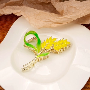 Detail of golden wheat-shaped hair claw clip with yellow enamel and green leaves