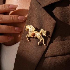 Detail view of the golden horse brooch pinned on a textured brown blazer lapel