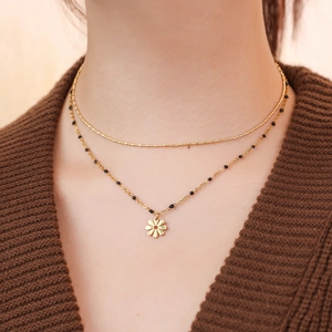 Close-up of double layer gold necklace with black beads and daisy flower pendant on a model