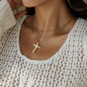 Close-up of double-layer gold necklace featuring a baroque pearl cross pendant