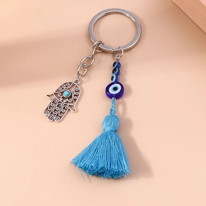 Hamsa Hand Evil Eye Keychain with blue tassels and silver metal charms on pink background