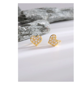 Close-up of gold heart stud earrings with sparkling white zircons on a natural stone base