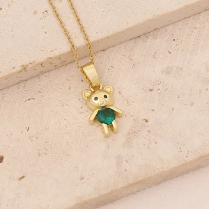 Macro view of golden bear pendant necklace with green gemstone on beige stone