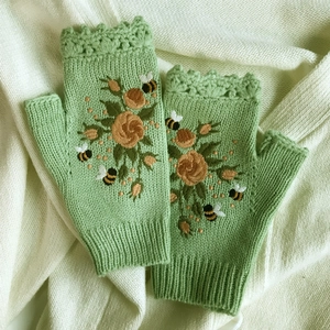Close-up of light green knit fingerless gloves featuring rose and bee embroidery detail