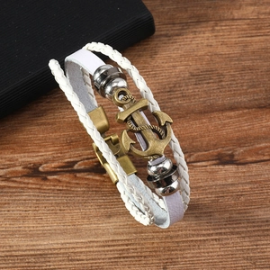 Close-up of multilayer white leather bracelet with bronze anchor on dark wood background