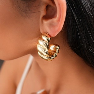 Polished gold twisted C-shape hoop earrings worn by a model in warm elegant lighting