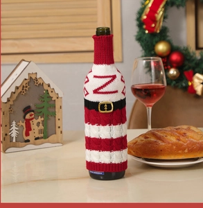 Close-up of a festive knitted Santa belt wine bottle cover on a warm Christmas dinner table