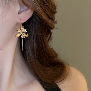 Detailed view of elegant gold iris flower earrings worn by a model with metal texture
