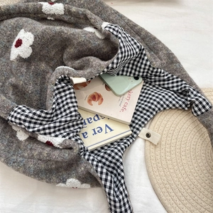 Macro detail of plush knit tote bag showing grey floral embroidery and plaid cotton lining