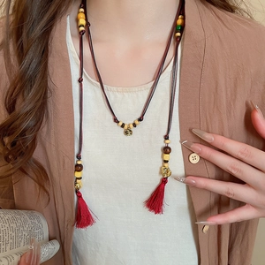 Close-up of ethnic beaded belt necklace with red silk tassels and retro metal pendant