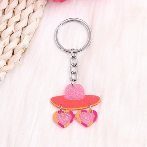 Détail du porte-clés chapeau rose pailleté et lunettes cœur sur fausse fourrure blanche