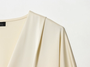 Détail d'un chemisier en satin beige avec col en V, plis aux épaules et étiquette