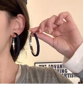 Detail of oversized hoop earrings wrapped in dark blue denim fabric on ear