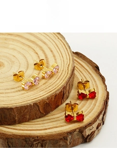 Close-up of gold bow earrings with pink and red heart zircons on wooden stand