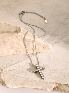 Macro detail of silver cross pendant with clear zircons on a snake chain over beige rock